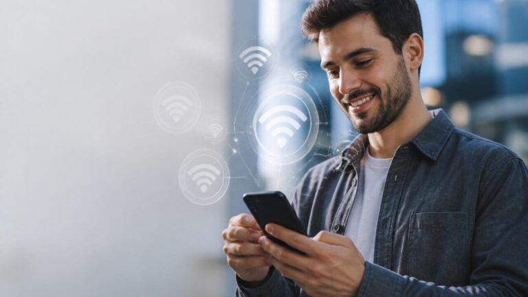 Pessoa segurando smartphone com ícones de redes Wi‑Fi flutuando ao redor, em ambiente moderno e neutro.